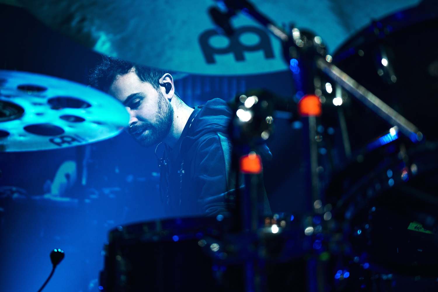 Miguel Lamas at the drums under blue stage light, DREAM in-ear monitor visible
